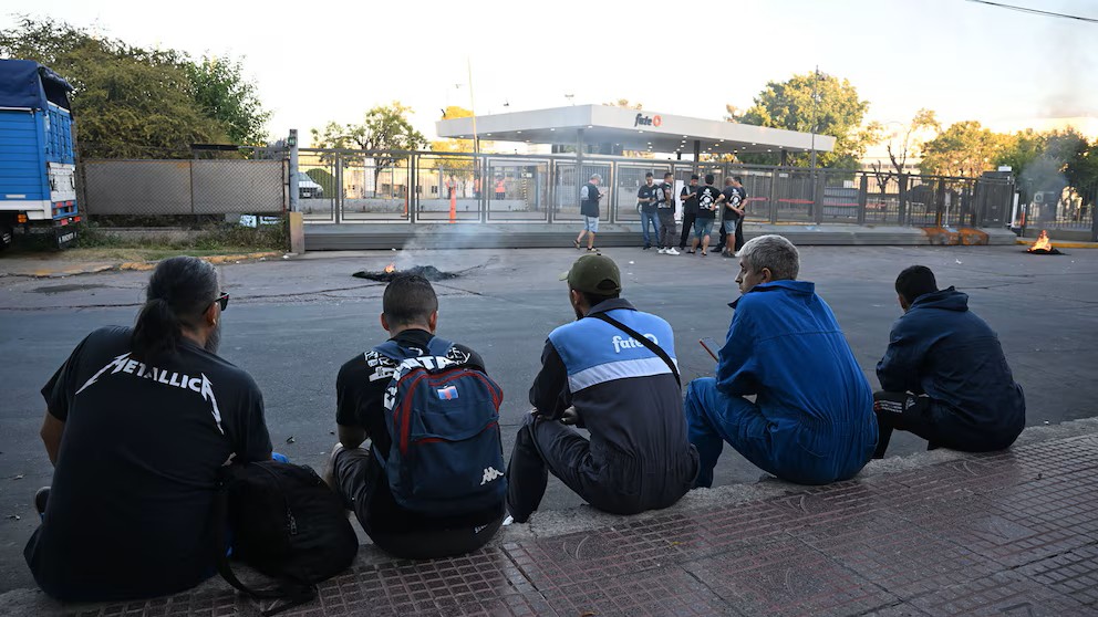 Un grupo de trabajadores se sienta en la vereda frente a la planta de Fate. (Crédito: Infobae - Maximiliano Luna)